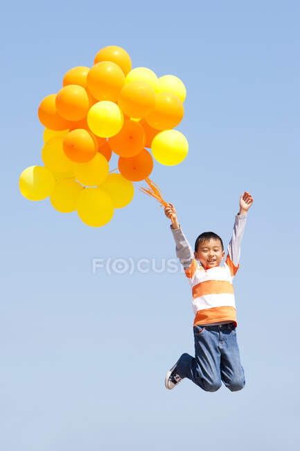 Menino chinês jovem pulando com balões — Fotografia de Stock