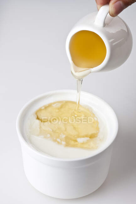 Hand gießt Honig in Joghurt aus Krug — Stockfoto