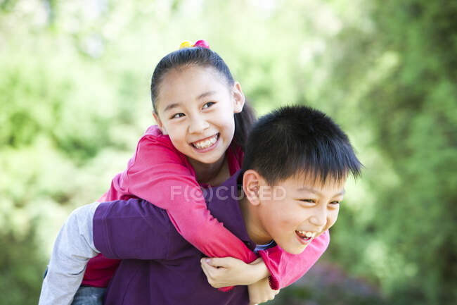 Young Chinese boy giving girl piggyback ride — Stock Photo