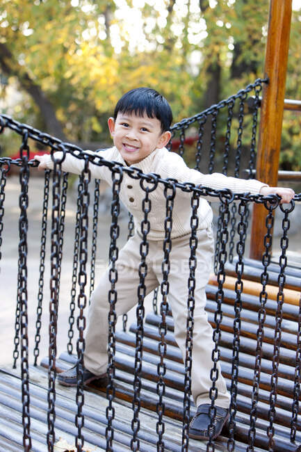 Chino niño jugando en parque infantil juguete puente - foto de stock