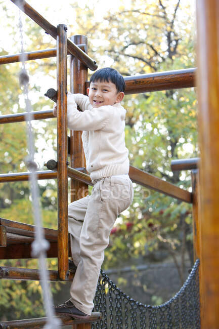 Rapaz chinês a subir uma escada num parque infantil — Fotografia de Stock