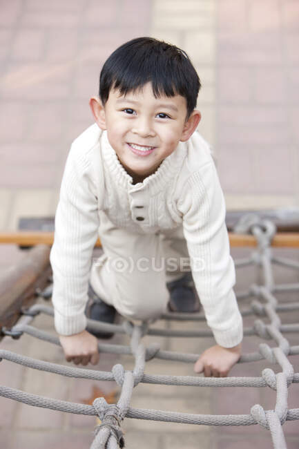 Chinese boy climbing playground rope ladder — Stock Photo