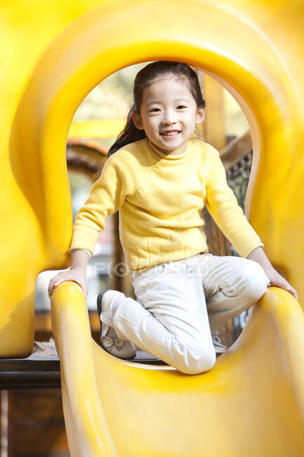 Chica china jugando en la diapositiva del patio - foto de stock