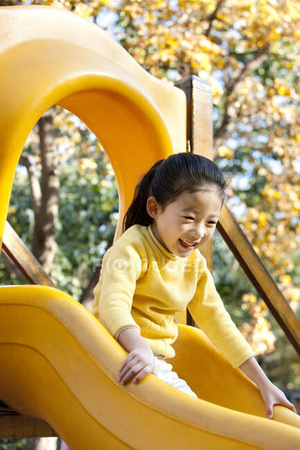 Chica china jugando en la diapositiva del patio - foto de stock