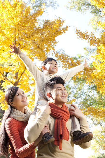 Menino chinês sentado nos ombros de seu pai em um parque com a família no outono — Fotografia de Stock