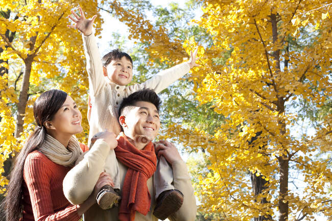 Chinese boy sitting on his father's shoulders in a park with family in autumn — Stock Photo