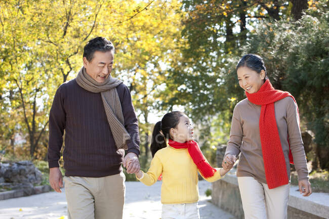 Senior Chinese couple with granddaughter strolling through the park in autumn — Stock Photo