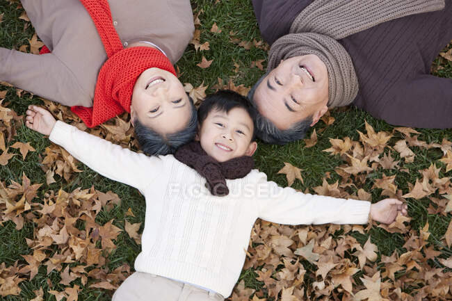 Chico chino con abuelos tumbados en la hierba en otoño - foto de stock