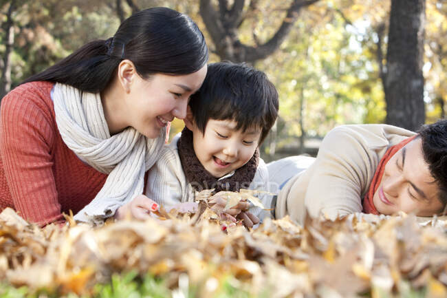 Young Chinese family lying on the grass surrounded by autumn leaves — Stock Photo