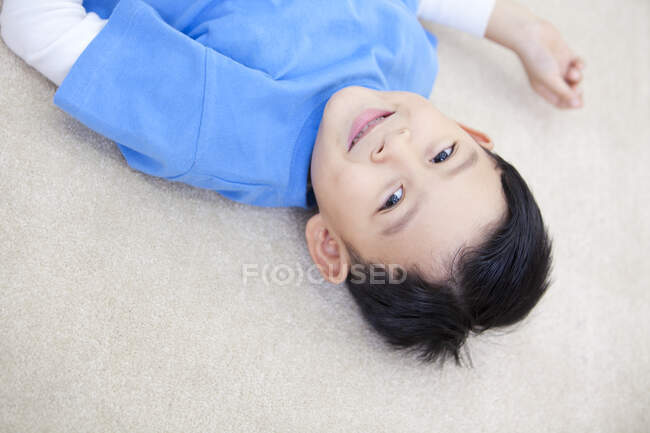 Улыбающийся китайский мальчик лежит на полу — стоковое фото