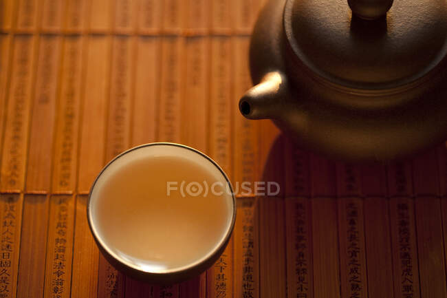 Tea in cup and pot on wooden mat — Stock Photo