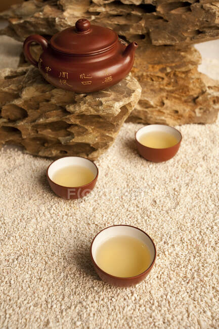 Set de té en maceta y tazas en la superficie de roca y arena - foto de stock