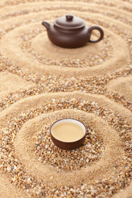 Taza de té llena y olla en la superficie de arena - foto de stock
