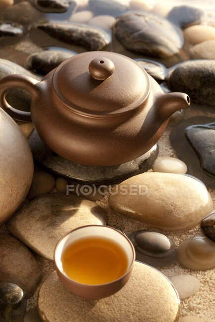 Teekanne und Tasse mit Kieselsteinen im Wasser — Stockfoto