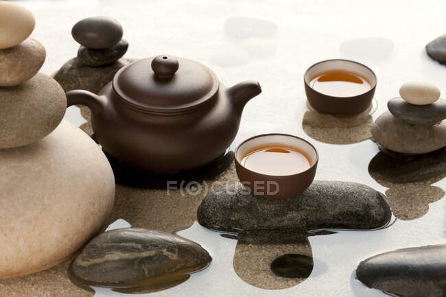 Conjunto de tazas de té y olla y guijarros en agua - foto de stock