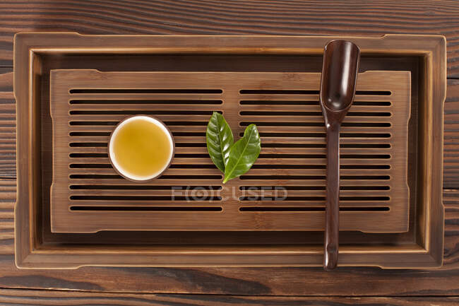 Tè in tazza, foglie verdi e paletta di legno — Foto stock