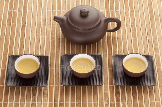 Chinesische Keramik-Tee-Set mit Kanne und gefüllten Tassen auf Bambusmatte — Stockfoto