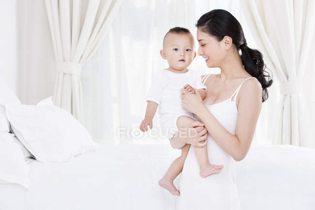 Chinese mother holding baby boy in bedroom — Stock Photo