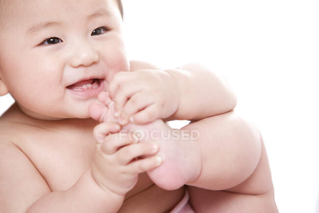 Cheerful Chinese baby girl holding her foot — Stock Photo
