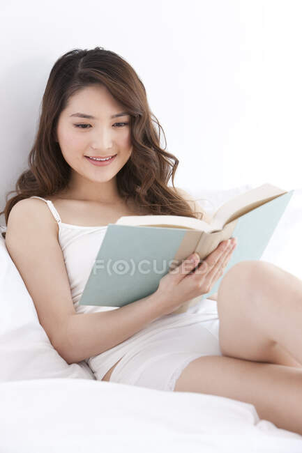 Молодая китаянка читает книгу в постели — стоковое фото