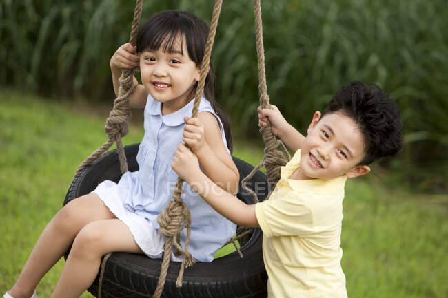 Cheerful Chinese children playing on a swing — Stock Photo