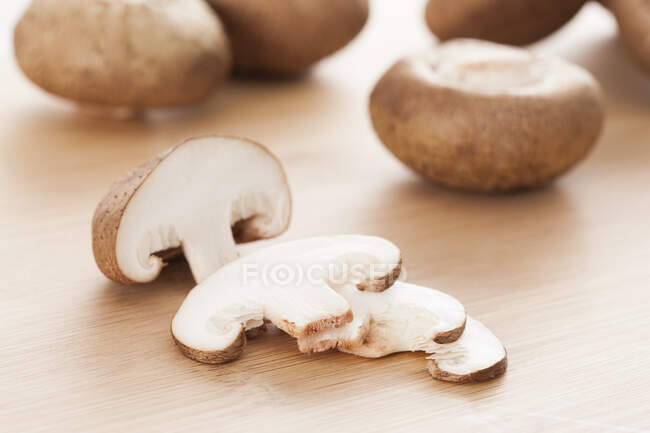 Funghi shiitake interi e tagliati a fette su superficie di legno — Foto stock