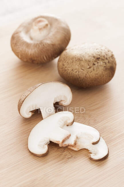Cogumelos Shiitake inteiros e picados em tábua de corte de madeira — Fotografia de Stock