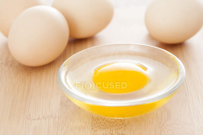 Whole eggs on wooden board with bowl of liquid egg — Stock Photo