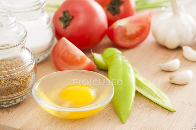 Ingredients for cooking on wooden board, garlic, egg in bowl and tomatoes — Stock Photo