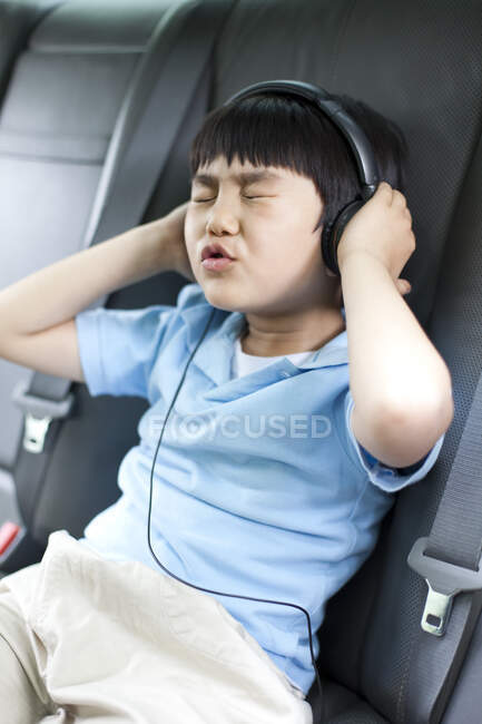 Cute Chinese boy listening to music and singing in car — Stock Photo