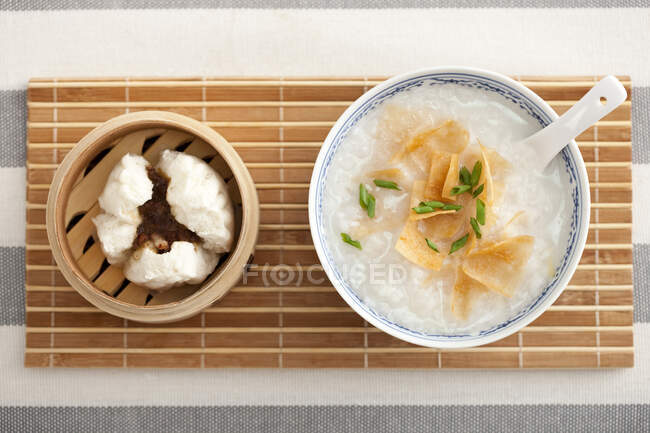 Tazón de gachas de arroz y bollos al vapor servidos en la mesa - foto de stock