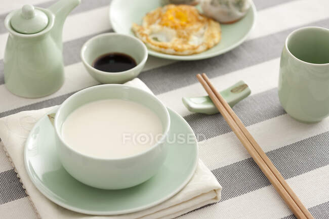 Leche de soja con alimentos y palillos servidos en la mesa - foto de stock