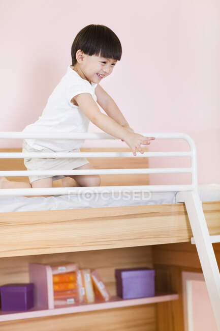 Linda chica china sentada en la cama y saludando - foto de stock