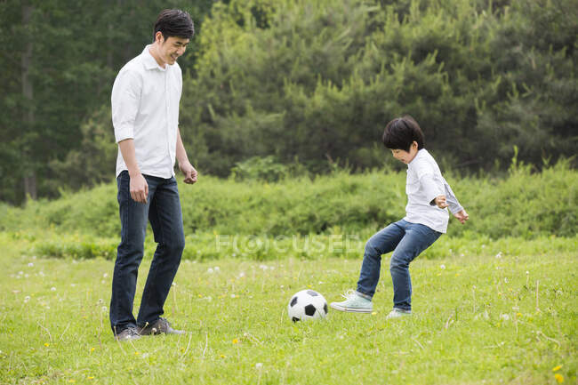 Happy Chinese father and son playing football together — Stock Photo