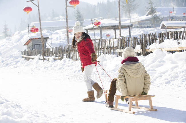 Enfants chinois heureux jouant avec traîneau dans la neige — Photo de stock