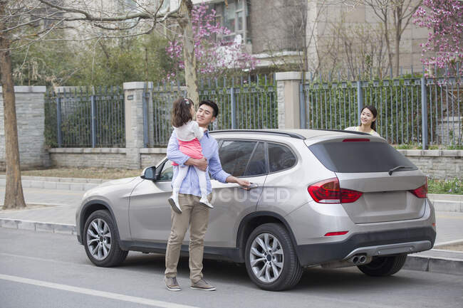 Happy Chinese father opening car door with daughter in his arms — Stock Photo
