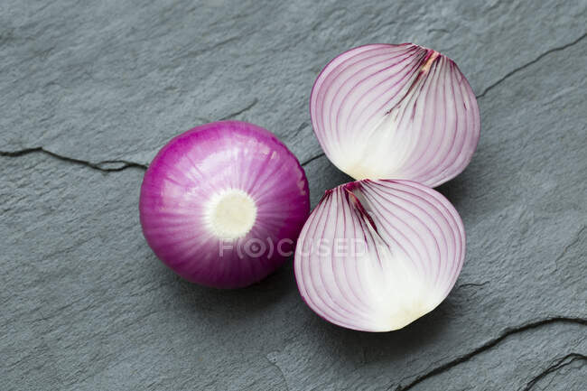 Fresh whole and halved red onions on slate surface — Stock Photo