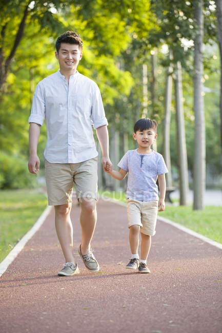 Padre e hijo chinos caminando juntos en el parque - foto de stock