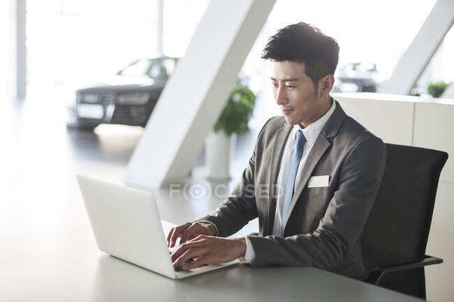 Молодой китайский бизнесмен работает с ноутбуком в офисе — стоковое фото