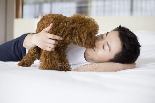 Young Chinese man playing with a pet poodle at home — Stock Photo