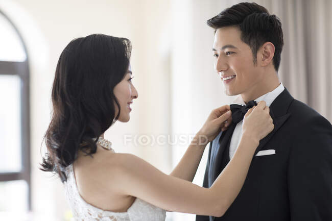 Joven esposa china ajustando corbata de lazo para su marido - foto de stock