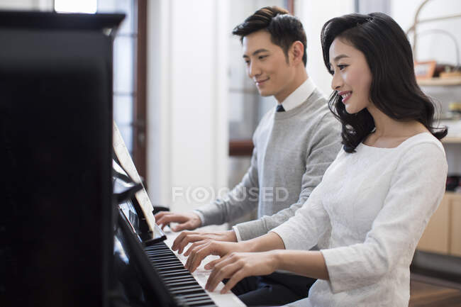 Noble young Chinese couple playing the piano together — Stock Photo