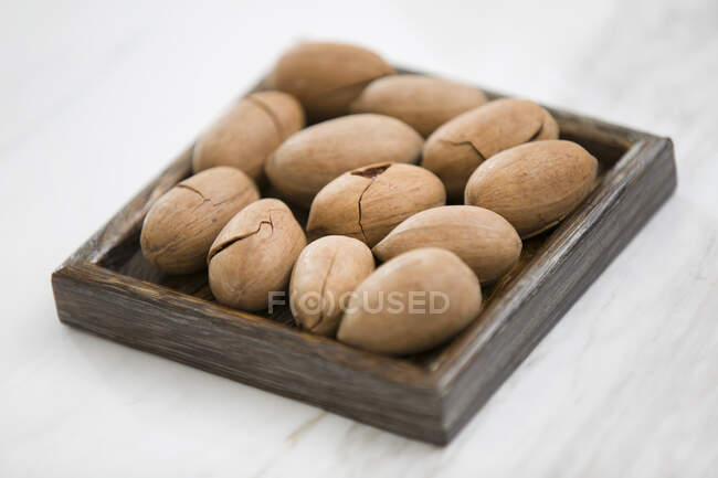 Pecans on square wooden plate on white wooden surface — Stock Photo