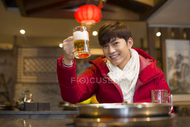 Молодой китаец пьет пиво в горячем ресторане — стоковое фото
