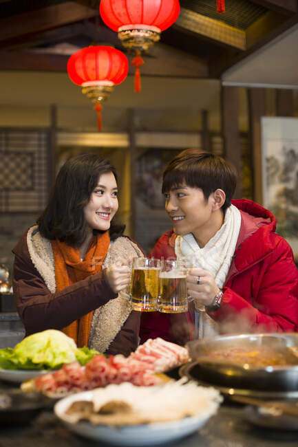 Молодая китайская пара пьет пиво в ресторане с горячим баром — стоковое фото