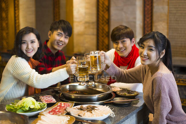 Jóvenes amigos chinos bebiendo cerveza en el restaurante hotpot - foto de stock