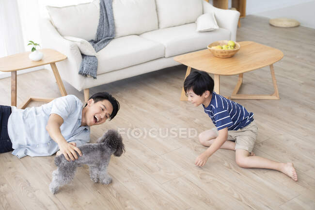 Chinesischer Vater und Sohn spielen mit Hund auf dem Boden — Stockfoto