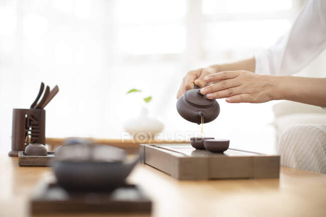 Tiro cortado de mulher derramando chá em copos de panela de cerâmica — Fotografia de Stock