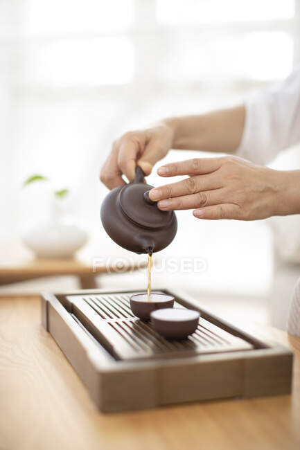 Colpo ritagliato di donna versando il tè in tazze da pentola di ceramica — Foto stock