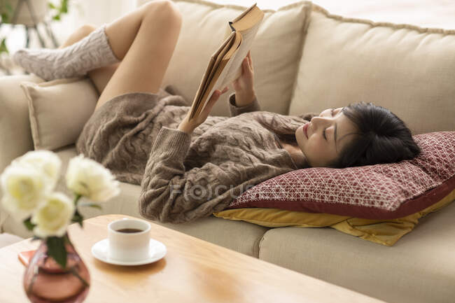 Jovem chinesa leitura livro no sofá — Fotografia de Stock